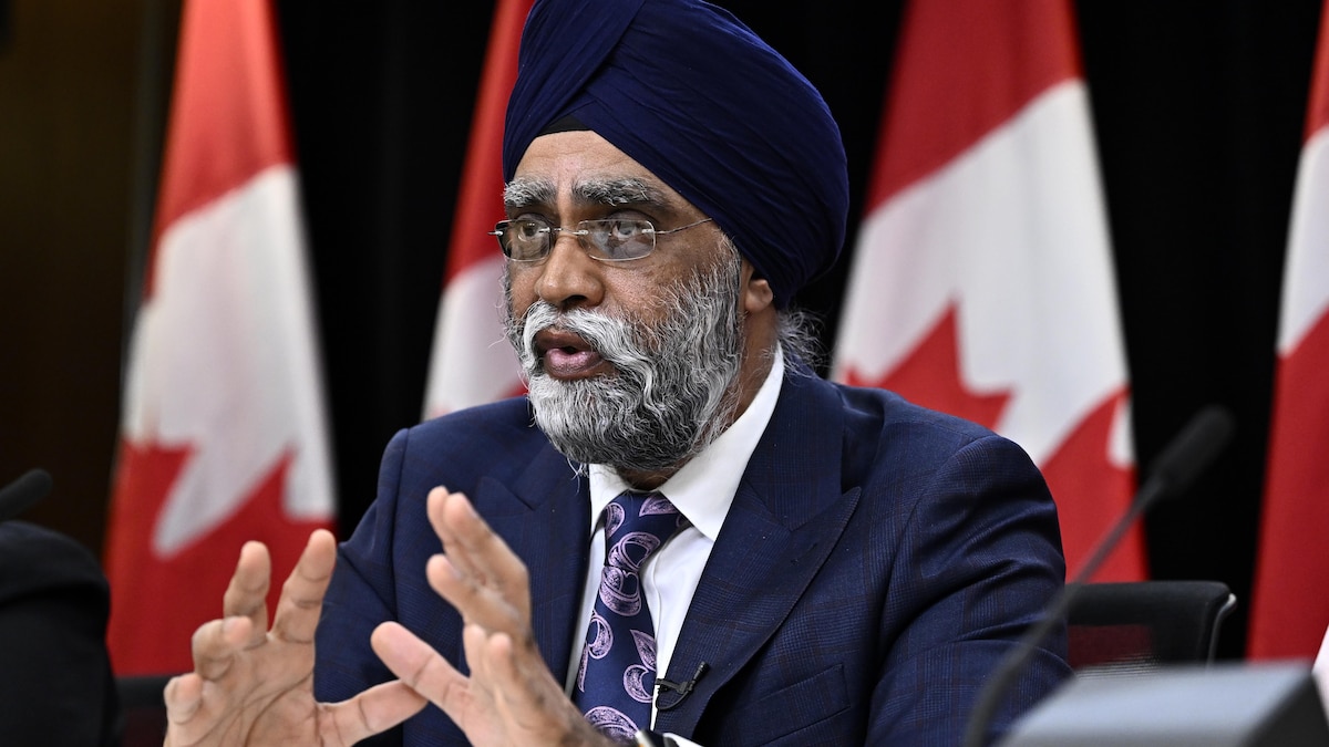 Le ministre canadien de la Protection civile, Harjit Sajjan, prend la parole lors d'une conférence de presse devant des drapeaux canadiens.