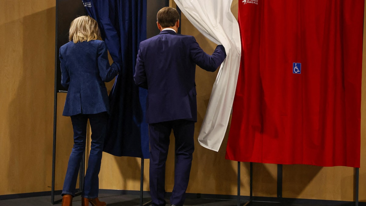Un homme et une femme soulèvent chacun un rideau d'isoloir dans un bureau de vote.