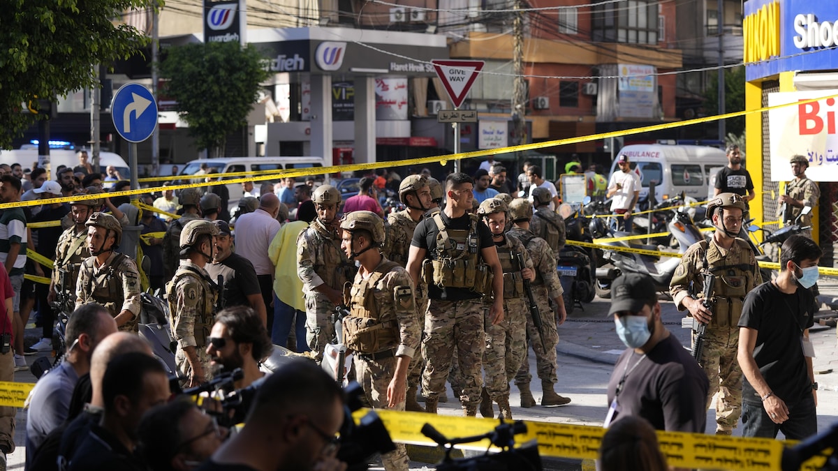 Des soldats et des civils (tous des hommes), se pressent dans une rue à l'intérieur d'un périmètre de sécurité. Une ambulance est sur les lieux.