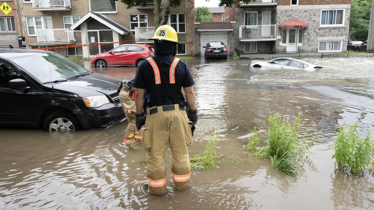 Deux pompiers regardent une rue inondée.