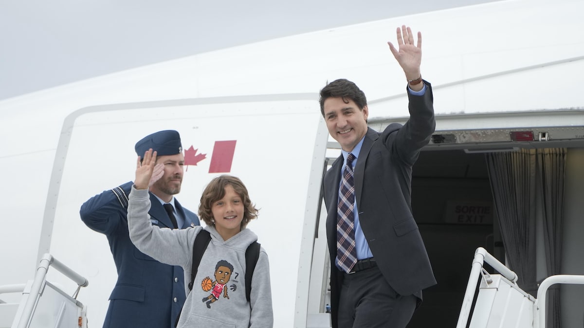 Justin Trudeau et son fils envoient une main dans les airs, devant la porte d'un avion.