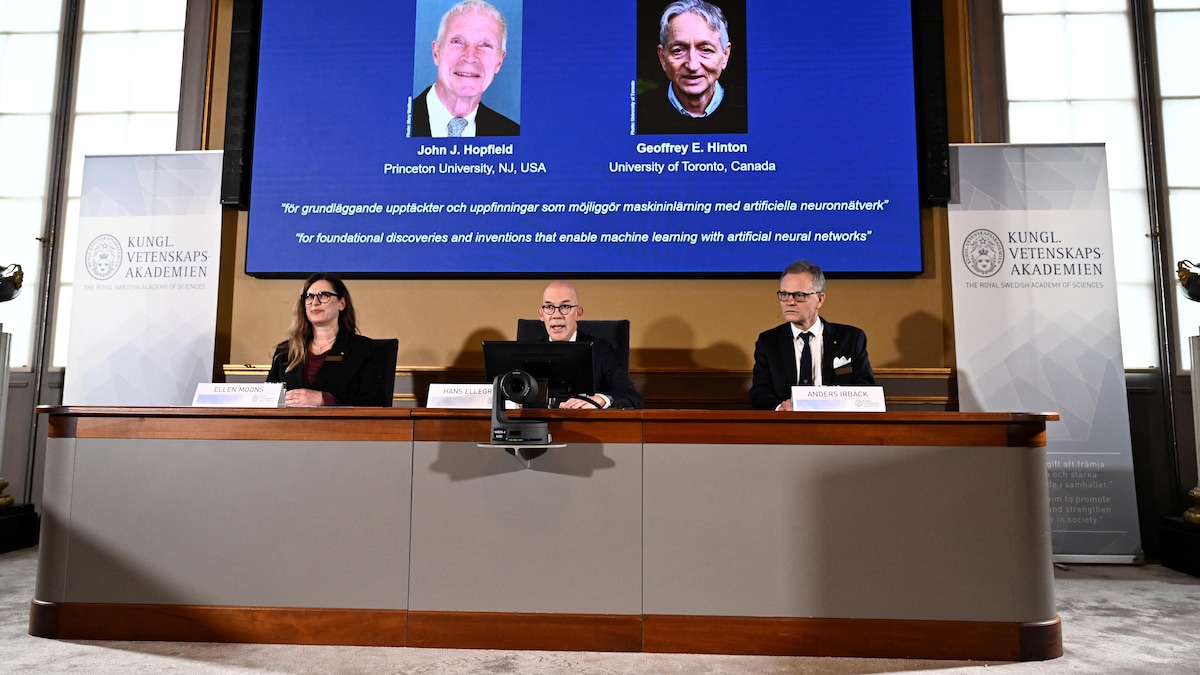 Un homme, au centre d'une femme et d'un homme, annonce les lauréats du prix Nobel de physique.