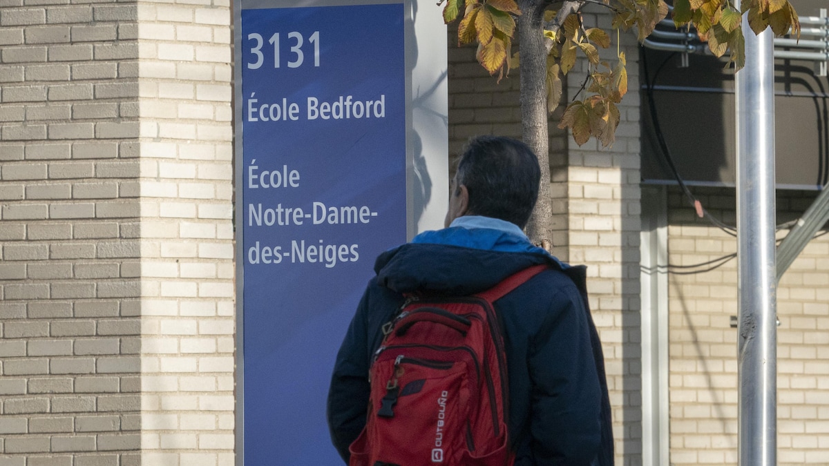 Un homme vu de dos regarde le panneau devant la façade de l'école primaire Bedford.