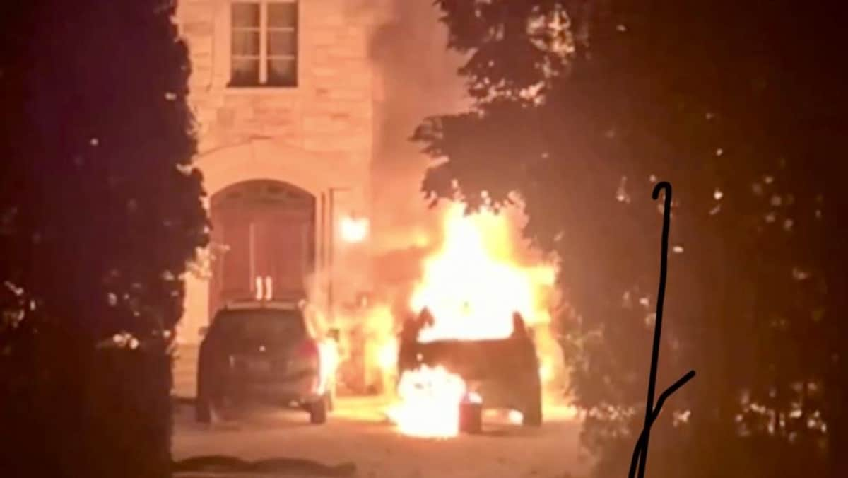 Une voiture en flammes devant une maison.