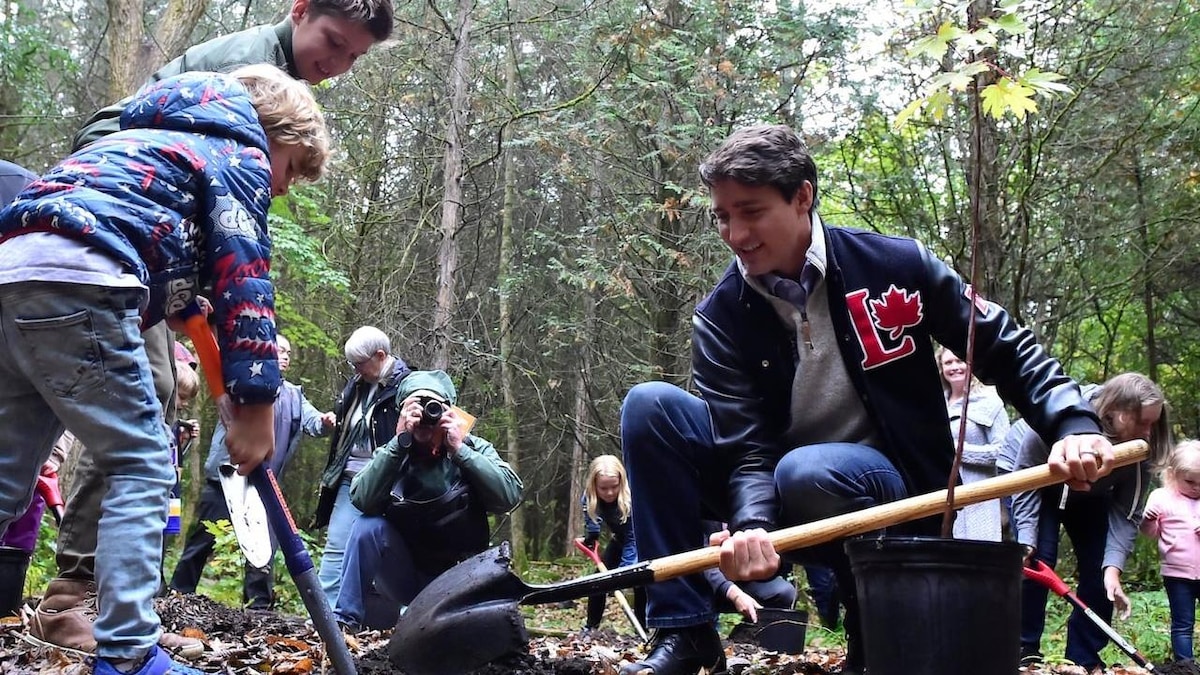 Dans une forêt, Justin Trudeau utilise une pelle, entouré d'enfants, dont ses fils.