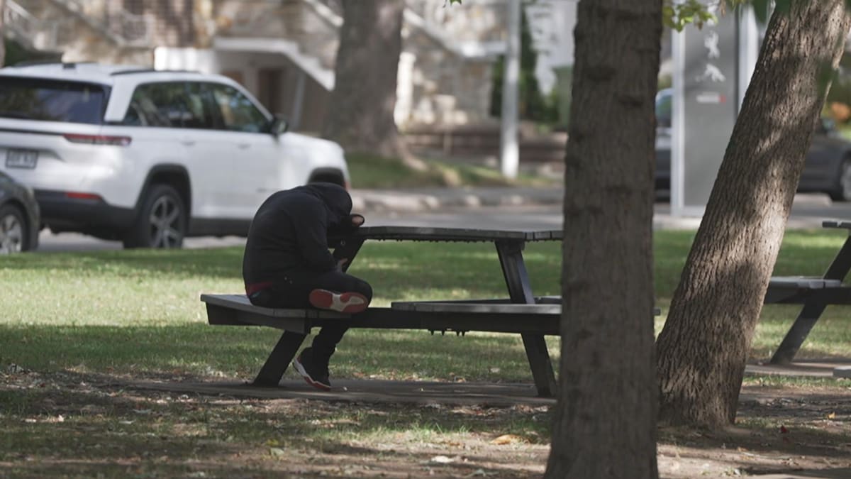 Un jeune assis à une table de pique-nique dans un parc pose sa tête sur la surface de bois de la table.