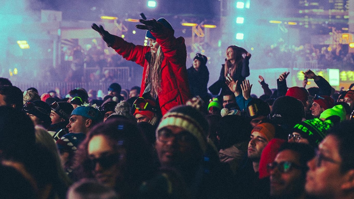 Une femme assise sur les épaules d'un homme parmi une grande foule qui assiste à un spectacle extérieur en hiver.