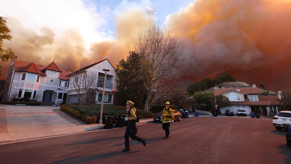 Des pompiers courent dans une rue menacée par les flammes.