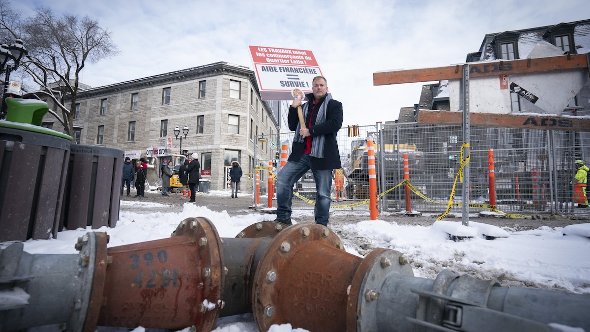 Devant un chantier dans la rue, Martin Guimond tient une pancarte réclamant de l'aide financière pour la survie des commercants.