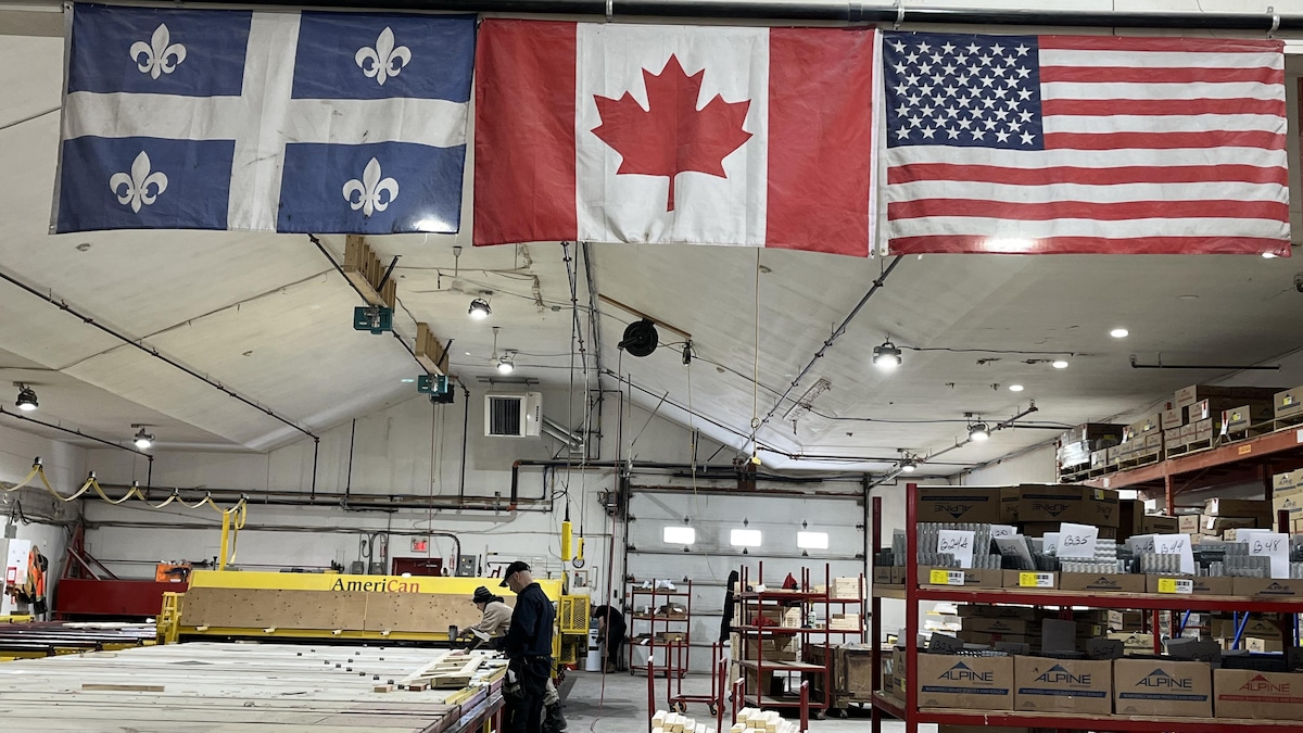 Les drapeaux du Québec, du Canada et des États-Unis sont accrochés au plafond d'une usine.